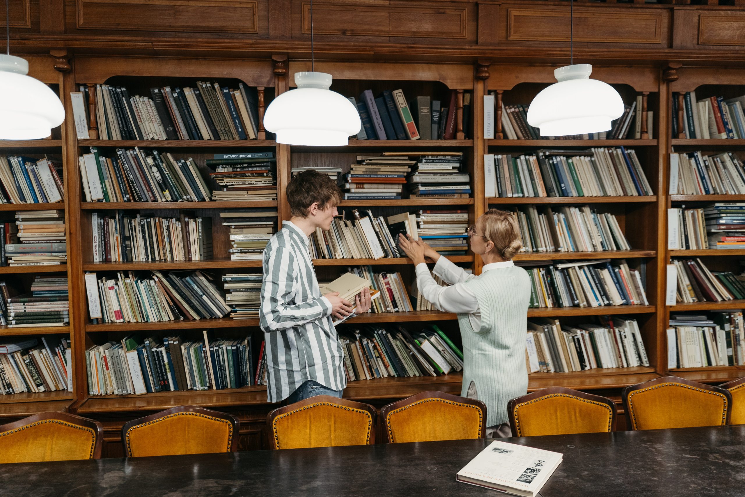Student and Teacher in front of a book shelf with cloud shaped lights hanging from the ceiling.