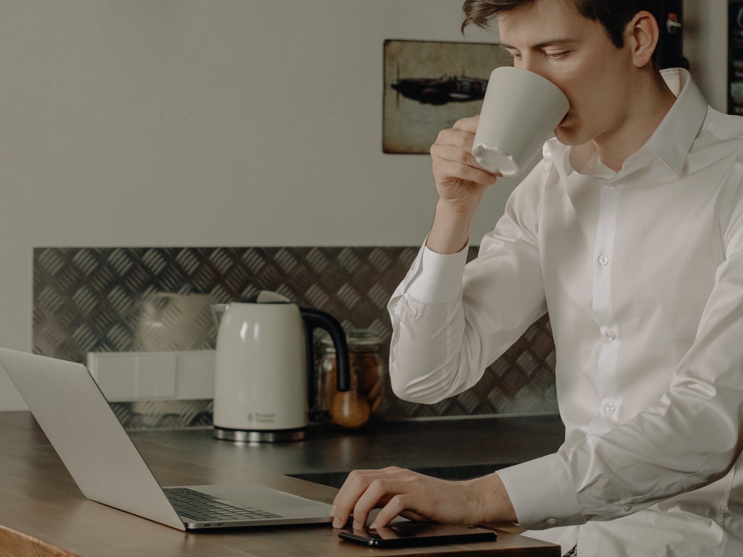 Person drinking something in front of the laptop in what does not appear to be a typical office to indicate work from home